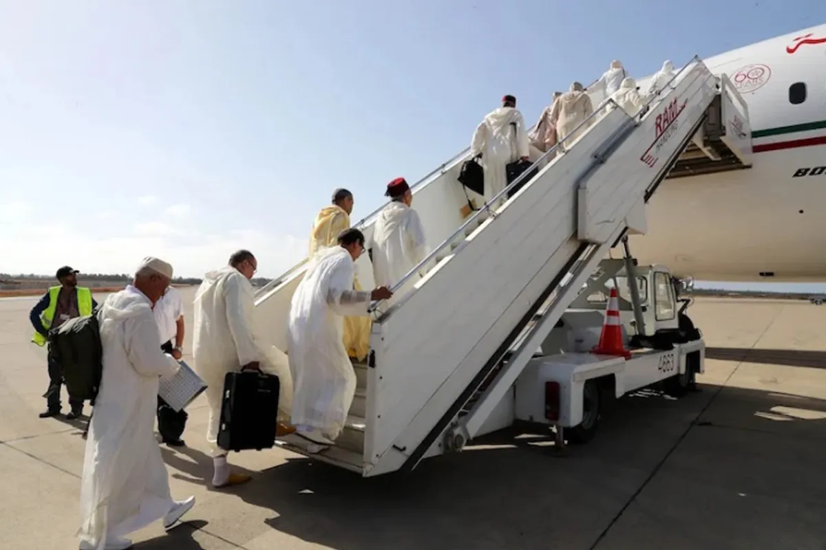الحجاج-المغاربة | MCG24 | موقع إلكتروني مغربي شامل متجدد على مدار الساعة Group of travelers in white robes ascend a mobile boarding stair to a plane on the tarmac, carrying bags and suitcases.