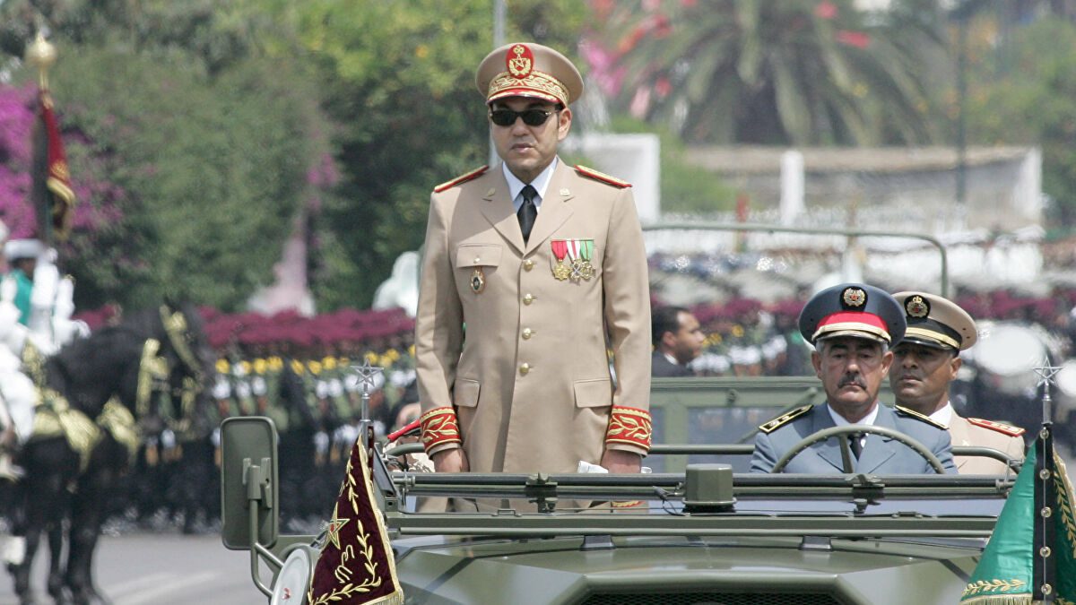 Uniformed officer standing in an open-top military vehicle during a parade, medals on his chest with other officers in the background.