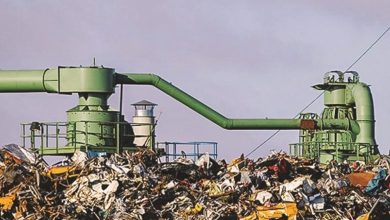 Industrial waste processing plant with large green pipes above a heap of garbage at a junkyard setting.
