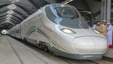 High-speed silver train at a station with engineers in beige uniforms and traditional white garments nearby in the background? (informative)