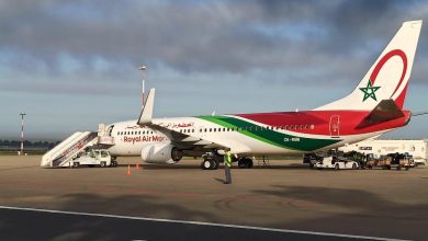 Royal Air Maroc passenger plane parked on the tarmac with mobile stairs connected to the front door and ground crew nearby including a worker in a high‑visibility vest.