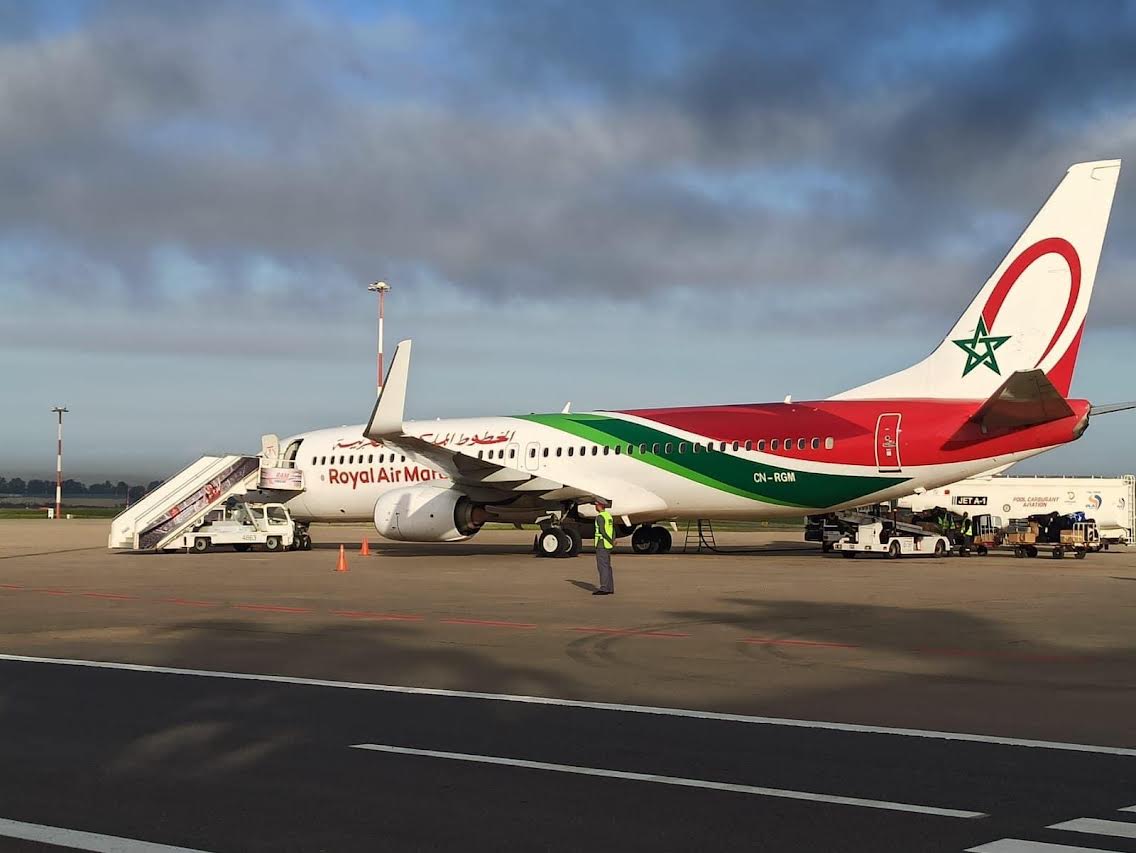 لارام | MCG24 | موقع إلكتروني مغربي شامل متجدد على مدار الساعة Royal Air Maroc passenger plane parked on the tarmac with mobile stairs connected to the front door and ground crew nearby including a worker in a high‑visibility vest.