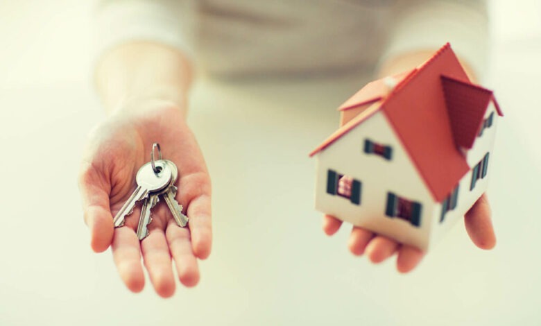 Hands holding a set of house keys and a small model red-roofed house, symbolizing home ownership or buying a home.