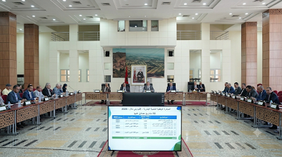 1000263336 | MCG24 | موقع إلكتروني مغربي شامل متجدد على مدار الساعة Large conference room with officials seated around U-shaped tables; a data presentation board sits at the front in the foreground.