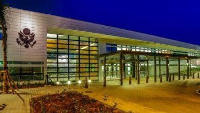 5487874 | MCG24 | موقع إلكتروني مغربي شامل متجدد على مدار الساعة Night exterior of a modern public building with a glass wall, emblem on the left, and a covered entrance.