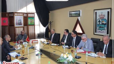 Group of officials in a formal meeting around a long conference table, Moroccan flag and crest visible in the room.