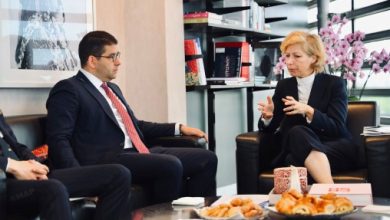 236572365732 | MCG24 | موقع إلكتروني مغربي شامل متجدد على مدار الساعة Two professionals in a modern office lounge, a man in a dark suit and red tie conversing with a woman in a dark blazer; pastries on the coffee table.