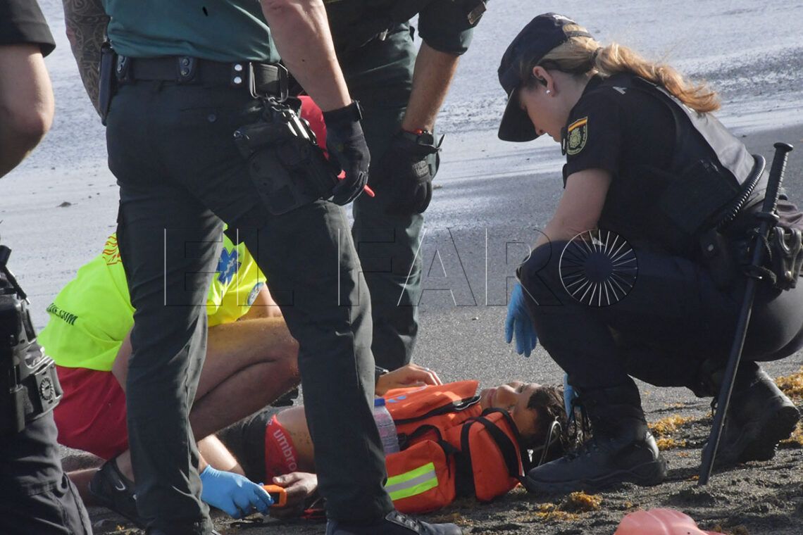 Emergency responders attend to a person lying on a beach, one rescuer checks the person’s airway while others prepare medical gear with gloves on.