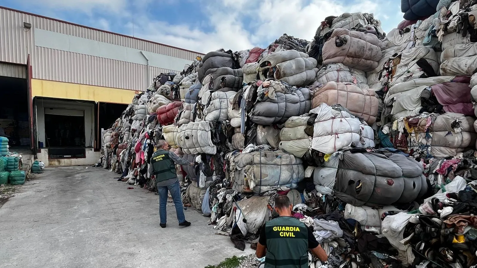 Guardia Civil officers inspect a massive pile of bundled clothes outside a warehouse.