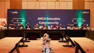 469 | MCG24 | موقع إلكتروني مغربي شامل متجدد على مدار الساعة Panel of officials seated at a long conference table on a stage, with a blue backdrop reading 'ANCA Executive Cybersecurity' and sponsor logos, and a floral arrangement in front.