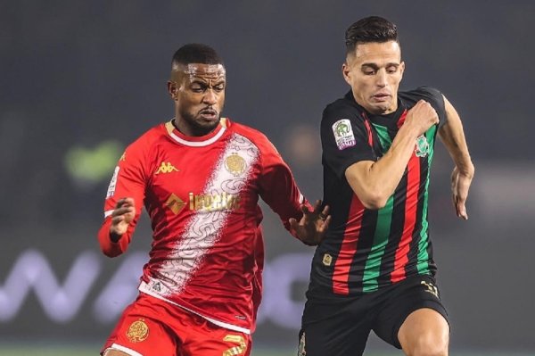 501973 | MCG24 | موقع إلكتروني مغربي شامل متجدد على مدار الساعة Two soccer players sprint toward the ball on a night match; one in red kit and the other in black with green and red stripes.