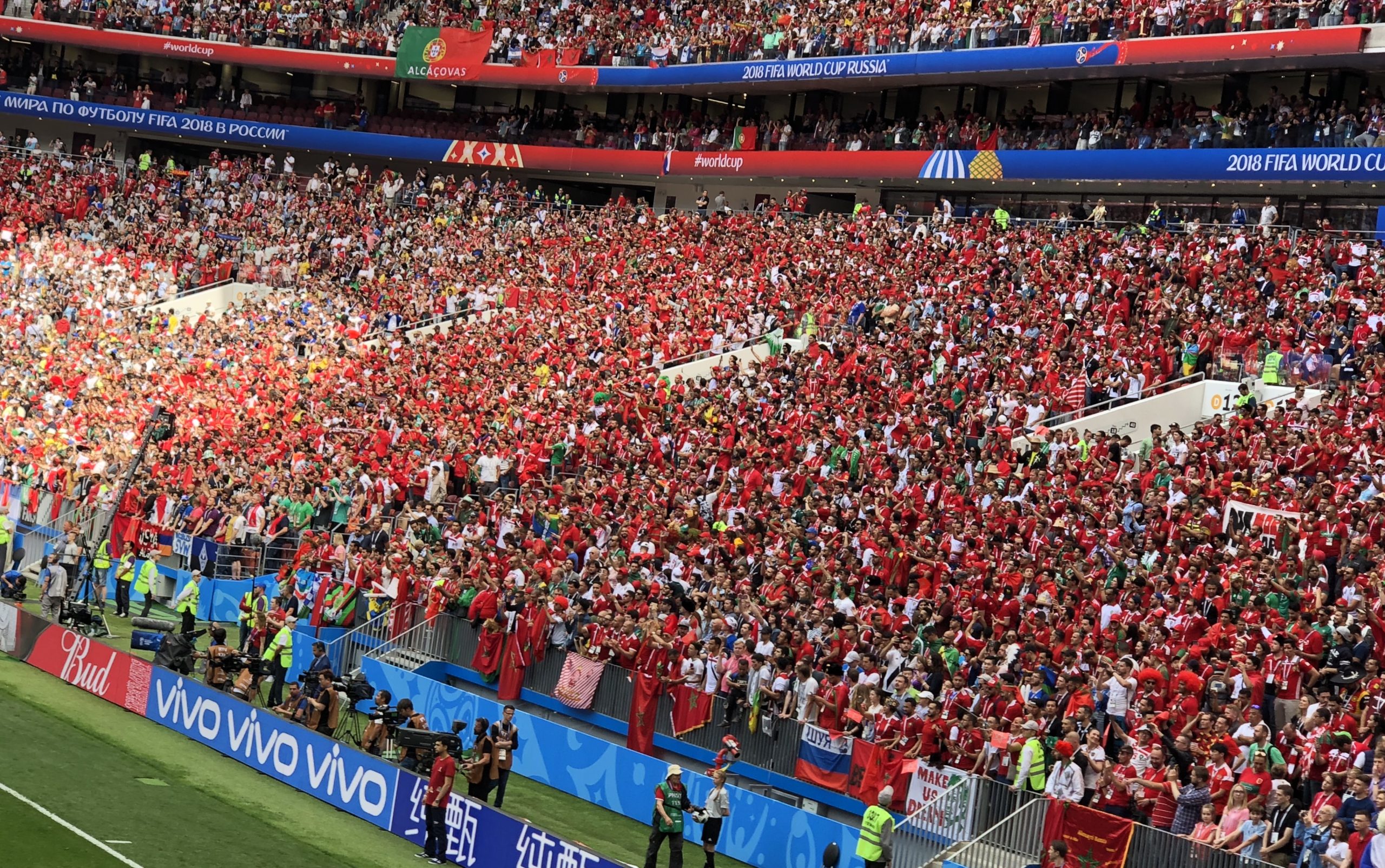Crowd of football fans wearing red shirts filling a stadium during a 2018 FIFA World Cup match with banners overhead reading Russia/Russia 2018 World Cup material]