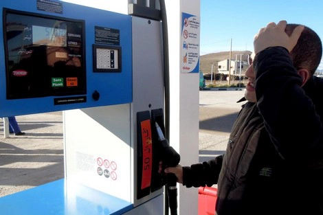 Man at a self-service gas pump, inserting a card at the reader while holding his head with one hand.
