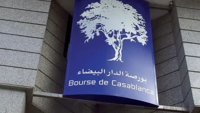 Blue vertical sign with a white tree logo and Arabic text, plus 'Bourse de Casablanca' in French, mounted on a gray stone wall.