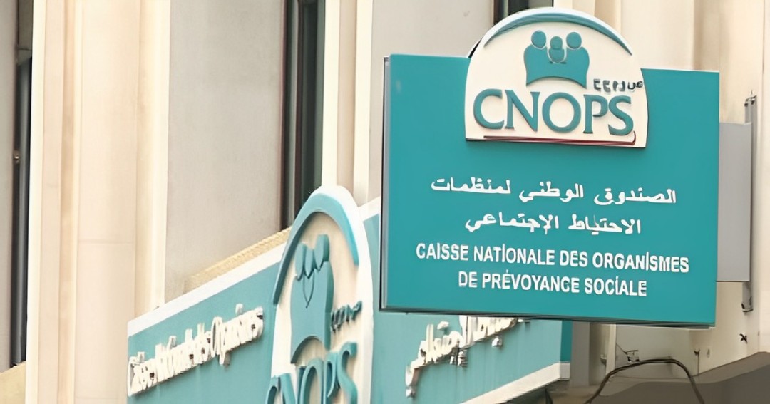 Signboard for CNOPS (Caisse Nationale des Organismes de Prévoyance Sociale) in teal with Arabic and French text on a building façade.