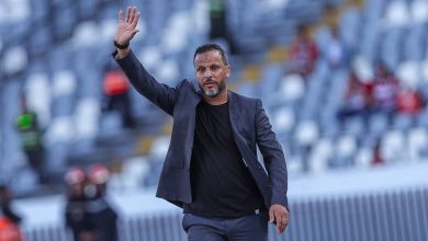 بنشريفة | MCG24 | موقع إلكتروني مغربي شامل متجدد على مدار الساعة Man in a dark blazer and black shirt waves while walking across a stadium field, with blurred empty seats in the background onlookers far away.