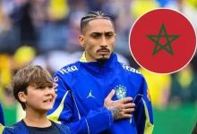 6a29c5ffa9193d59c3ee3594_default | MCG24 | موقع إلكتروني مغربي شامل متجدد على مدار الساعة Brazilian soccer player in a blue jacket with hand over heart stands beside a smiling boy on a soccer field, with a Morocco flag icon in the corner.