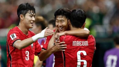 Three football players in red jerseys celebrate with arms around each other on the field, smiling. In the foreground, one wears number 3 and another has '6' on his back with 'INBEOM' visible on the jersey behind him.