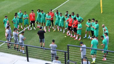 6a311ada6344e7d502f30810_default | MCG24 | موقع إلكتروني مغربي شامل متجدد على مدار الساعة Soccer team in green uniforms forming a circle around a coach giving instructions on a grassy practice field.