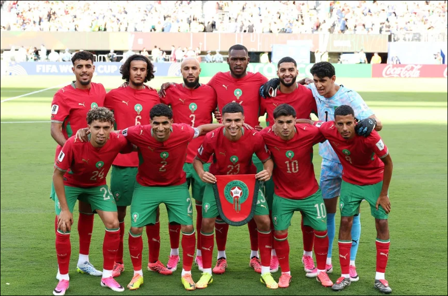 6a3439b057219 | MCG24 | موقع إلكتروني مغربي شامل متجدد على مدار الساعة Morocco national football team players pose for a pre-match photo on a green pitch, holding the team crest shield.