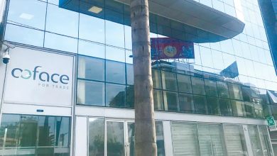 Glass-front office building with a Coface for Trade sign on the left and a palm tree in the foreground. There’s a banner with a smiley face overhead.