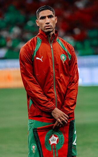 Achraf_Hakimi_ | MCG24 | موقع إلكتروني مغربي شامل متجدد على مدار الساعة Moroccan national football team player wearing a red-green training jacket on a soccer field.
