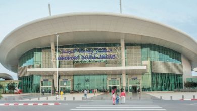 Aeroport-Oujda-Angad | MCG24 | موقع إلكتروني مغربي شامل متجدد على مدار الساعة Oujda Angads Airport terminal with a curved white roof, glass walls, and people walking toward the entrance under a clear sky.