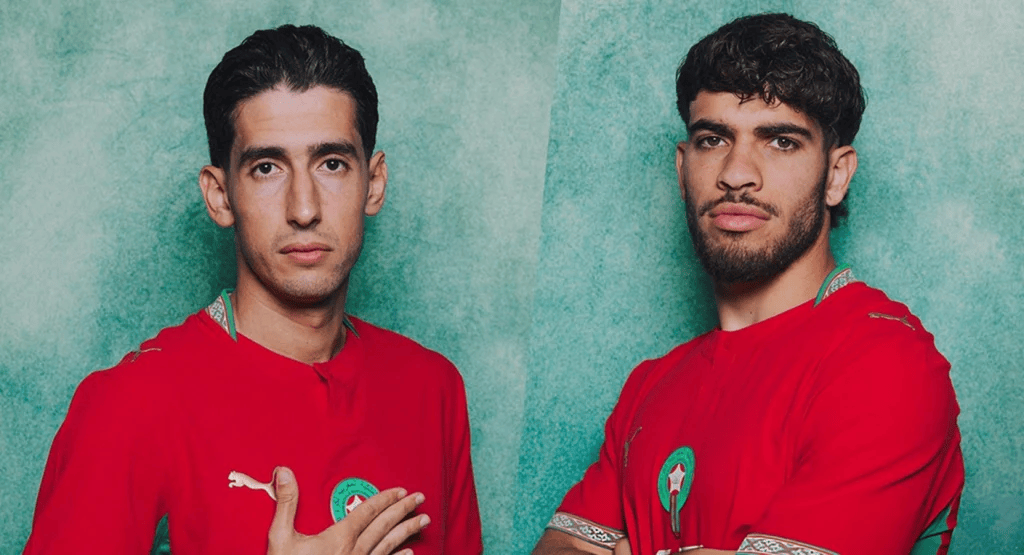 Aguerd-Zalzouli-Morocco-1 | MCG24 | موقع إلكتروني مغربي شامل متجدد على مدار الساعة Two men in red jerseys with green badges, standing against a green textured background, posing confidently side by side.