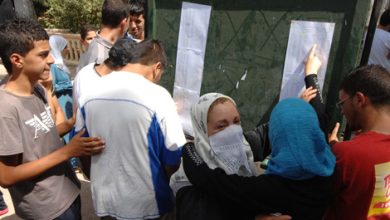 BAC_Resultats_03_317451583 | MCG24 | موقع إلكتروني مغربي شامل متجدد على مدار الساعة People gather around a green notice board with posted papers; two women in headscarves embrace while others look on.