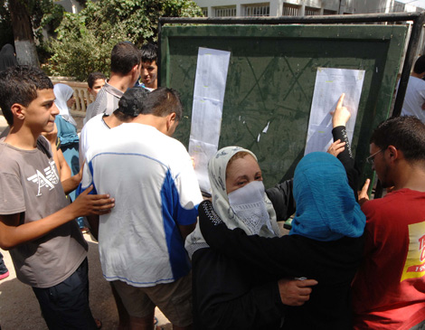 BAC_Resultats_03_317451583 | MCG24 | موقع إلكتروني مغربي شامل متجدد على مدار الساعة People gather around a green notice board with posted papers; two women in headscarves embrace while others look on.