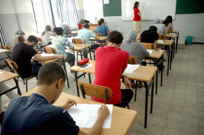 Bac | MCG24 | موقع إلكتروني مغربي شامل متجدد على مدار الساعة Students sit at individual desks in a classroom, taking a written exam as the teacher monitors from the front of the room.