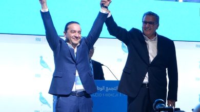 CHAOUKI | MCG24 | موقع إلكتروني مغربي شامل متجدد على مدار الساعة Two men in dark suits celebrate on stage, lifting their clasped hands in victory.