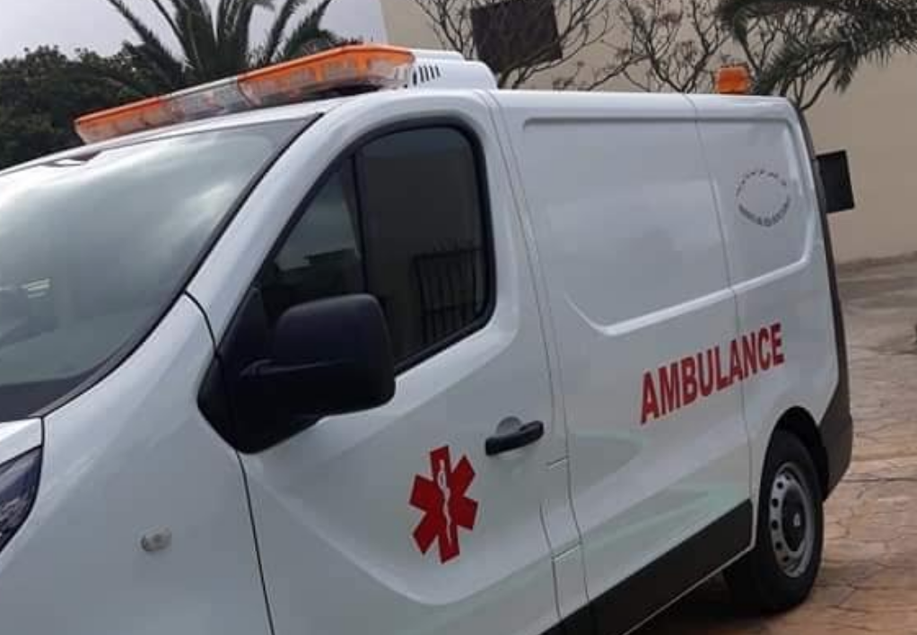 White ambulance van with orange emergency lights and 'AMBULANCE' text on the side.