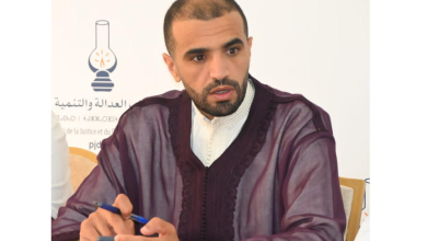 Capture-decran-2026-05-31-142553 | MCG24 | موقع إلكتروني مغربي شامل متجدد على مدار الساعة Man in a maroon traditional robe sits at a meeting, looking to the side while holding a phone and a pen.