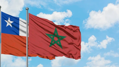 Chili-et-le-Maroc | MCG24 | موقع إلكتروني مغربي شامل متجدد على مدار الساعة Festive scene of two flagpoles with the Chilean flag (blue square with white star) next to the Moroccan flag (green pentagram) waving in the wind against a blue sky.