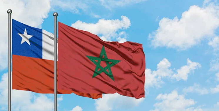 Chili-et-le-Maroc | MCG24 | موقع إلكتروني مغربي شامل متجدد على مدار الساعة Festive scene of two flagpoles with the Chilean flag (blue square with white star) next to the Moroccan flag (green pentagram) waving in the wind against a blue sky.