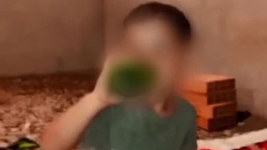 FB_IMG_1781557926180 | MCG24 | موقع إلكتروني مغربي شامل متجدد على مدار الساعة Blurred person wearing a gray shirt drinking from a green bottle in a cluttered room with cardboard boxes and a red blanket.