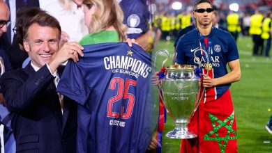 GettyImages-2278485465 | MCG24 | موقع إلكتروني مغربي شامل متجدد على مدار الساعة Two men on a soccer field celebrate a win: a man in a suit presents a blue jersey saying 'Champions of Europe' with the number 25 to a player beside a large silver trophy.