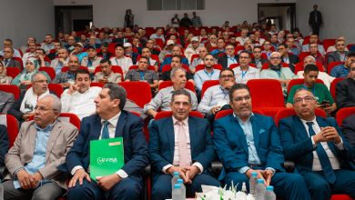 Audience of professionals seated in red chairs at a conference hall, many wearing badges and lanyards.