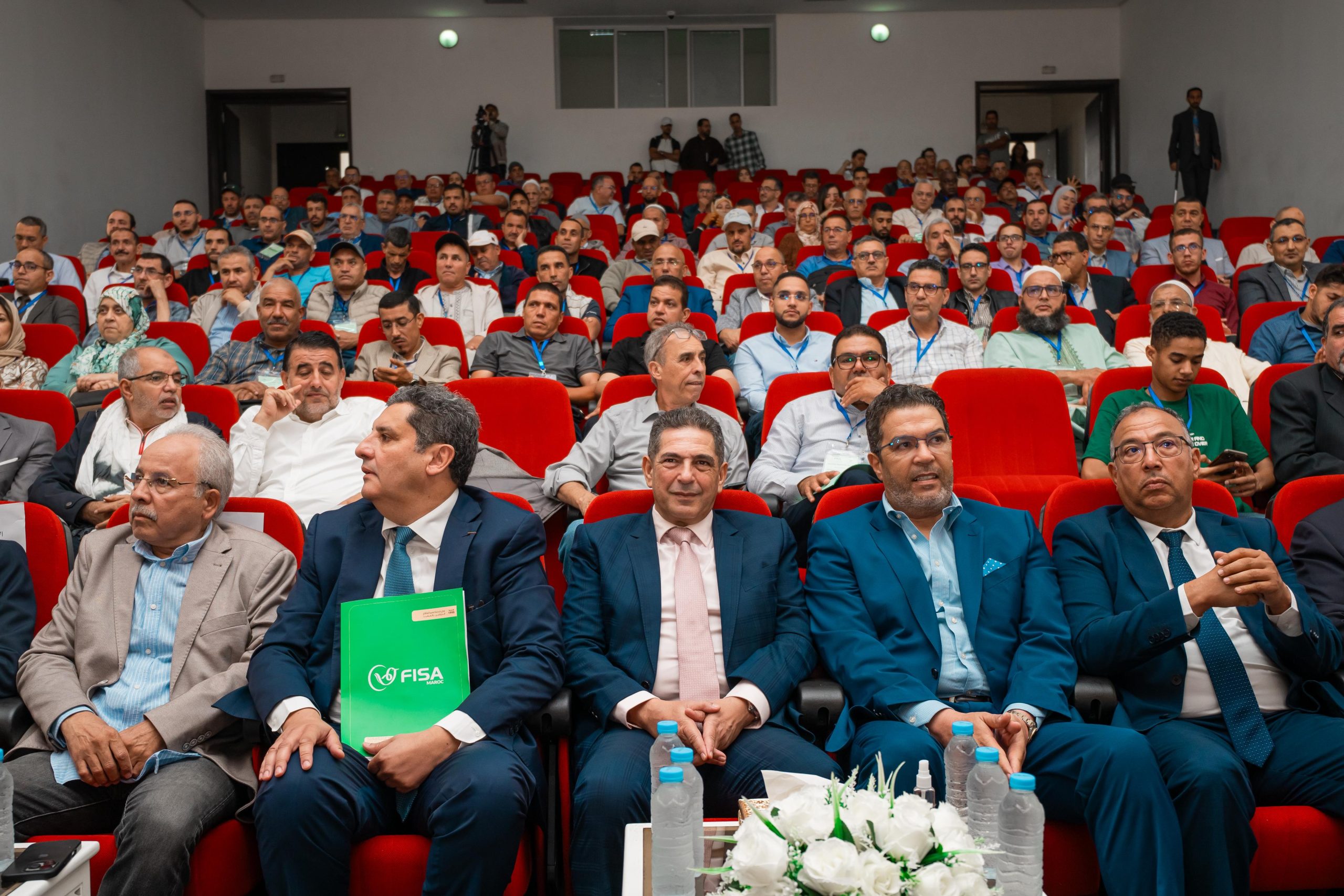 IMG-20260606-WA0059 | MCG24 | موقع إلكتروني مغربي شامل متجدد على مدار الساعة Audience of professionals seated in red chairs at a conference hall, many wearing badges and lanyards.