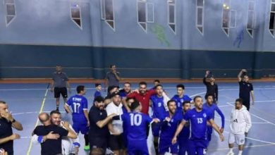 Indoor sports gym with a blue-clad team celebrating in a huddle after a game on a blue court with white lines.
