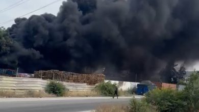 IMG-20260607-WA0147 | MCG24 | موقع إلكتروني مغربي شامل متجدد على مدار الساعة Thick black smoke rising from an industrial area beside a road, with a power line tower in the scene and a person walking nearby.