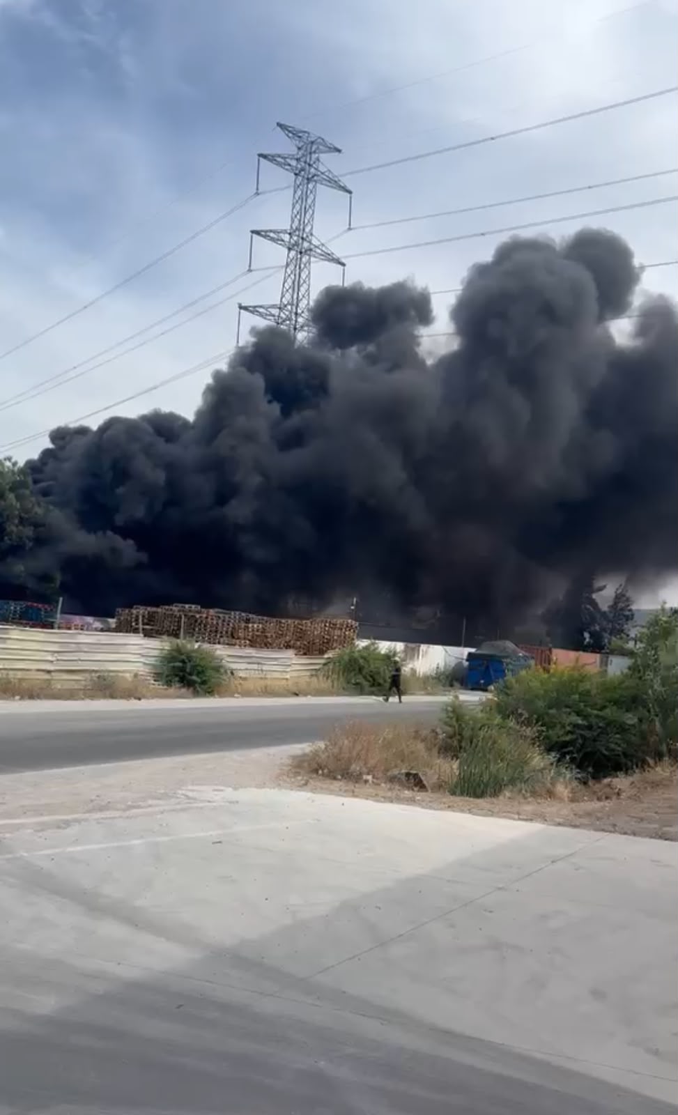 IMG-20260607-WA0147 | MCG24 | موقع إلكتروني مغربي شامل متجدد على مدار الساعة Thick black smoke rising from an industrial area beside a road, with a power line tower in the scene and a person walking nearby.