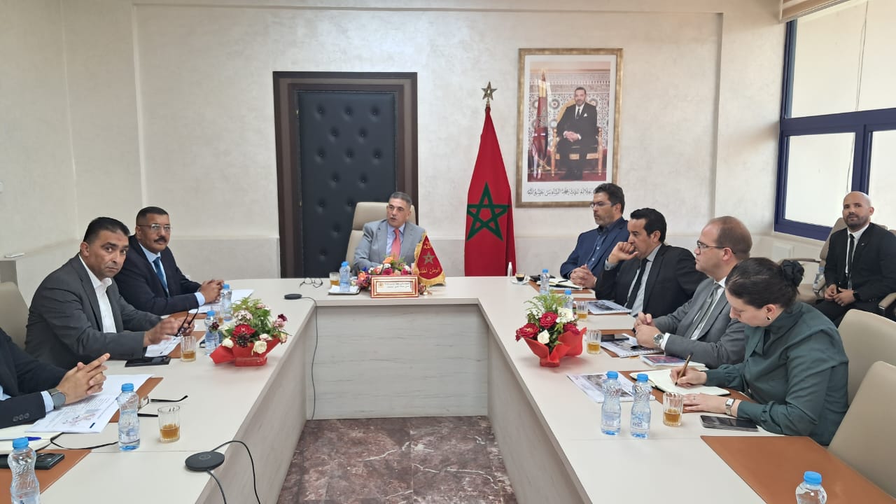 IMG-20260611-WA0333 | MCG24 | موقع إلكتروني مغربي شامل متجدد على مدار الساعة Official meeting in a Moroccan office: a man at the center speaks, with a Moroccan flag and framed portrait behind him, as attendees sit around a U-shaped conference table.