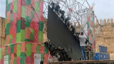 IMG-20260613-WA0041-1536x918-1 | MCG24 | موقع إلكتروني مغربي شامل متجدد على مدار الساعة Stage setup with a black screen prop being adjusted on scaffolding at a colorful FES Fanzone backdrop, worker on a platform