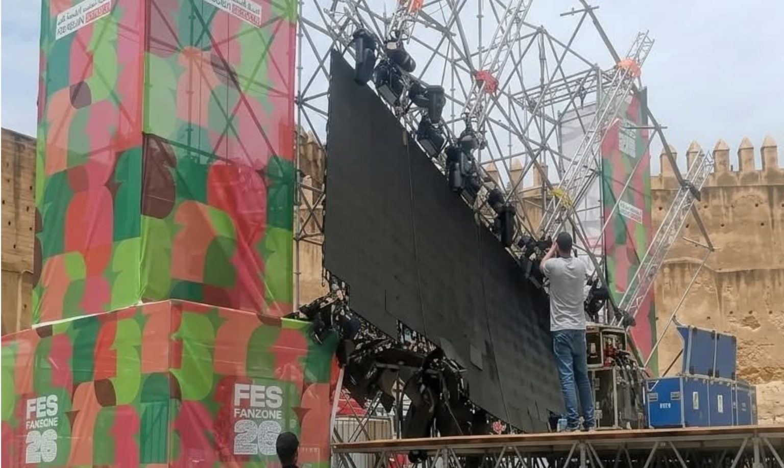 IMG-20260613-WA0041-1536x918-1 | MCG24 | موقع إلكتروني مغربي شامل متجدد على مدار الساعة Stage setup with a black screen prop being adjusted on scaffolding at a colorful FES Fanzone backdrop, worker on a platform