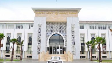 IMG-20260613-WA00451 | MCG24 | موقع إلكتروني مغربي شامل متجدد على مدار الساعة Front view of a modern government building with an arched entrance, palm trees, and a central fountain in front.