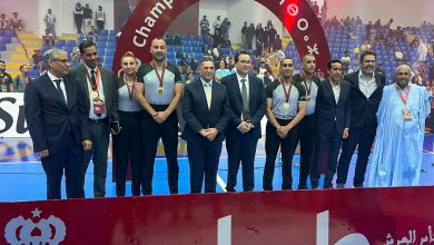 IMG-20260615-WA0075 | MCG24 | موقع إلكتروني مغربي شامل متجدد على مدار الساعة Group of medalists and officials posing on a sports court in front of a large red Champion arch and cheering crowd.