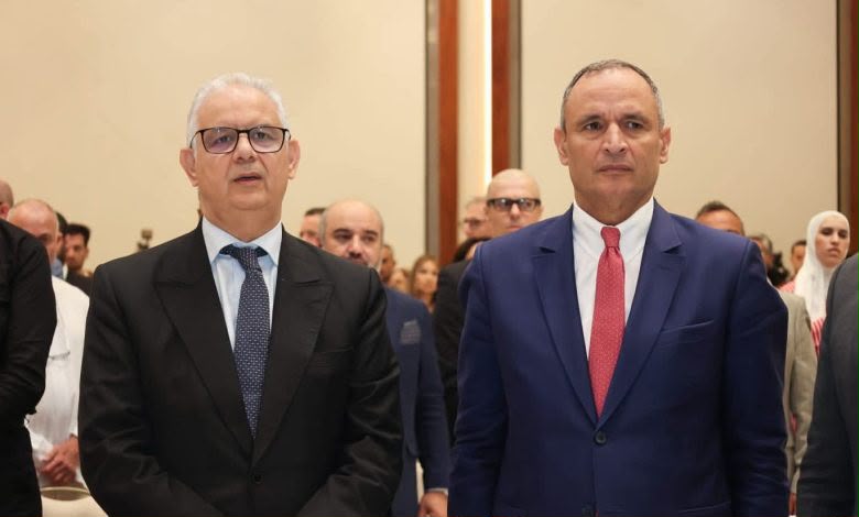 IMG-20260615-WA0096 | MCG24 | موقع إلكتروني مغربي شامل متجدد على مدار الساعة Two men in business suits standing at a formal event, with a crowd of attendees behind them in a conference hall.