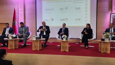 IMG-20260617-WA0007 | MCG24 | موقع إلكتروني مغربي شامل متجدد على مدار الساعة Five panelists seated on a stage in a formal discussion, with a Moroccan flag, flower arrangements, and a projection screen displaying Arabic stats behind them.
